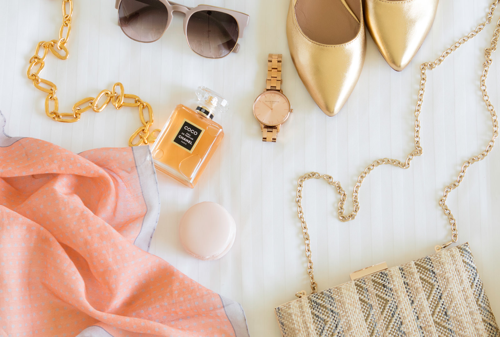 Scarf, sunglasses, perfume, watch, shoes, and purse laid on white bed from the Shops at the Grand America Hotel