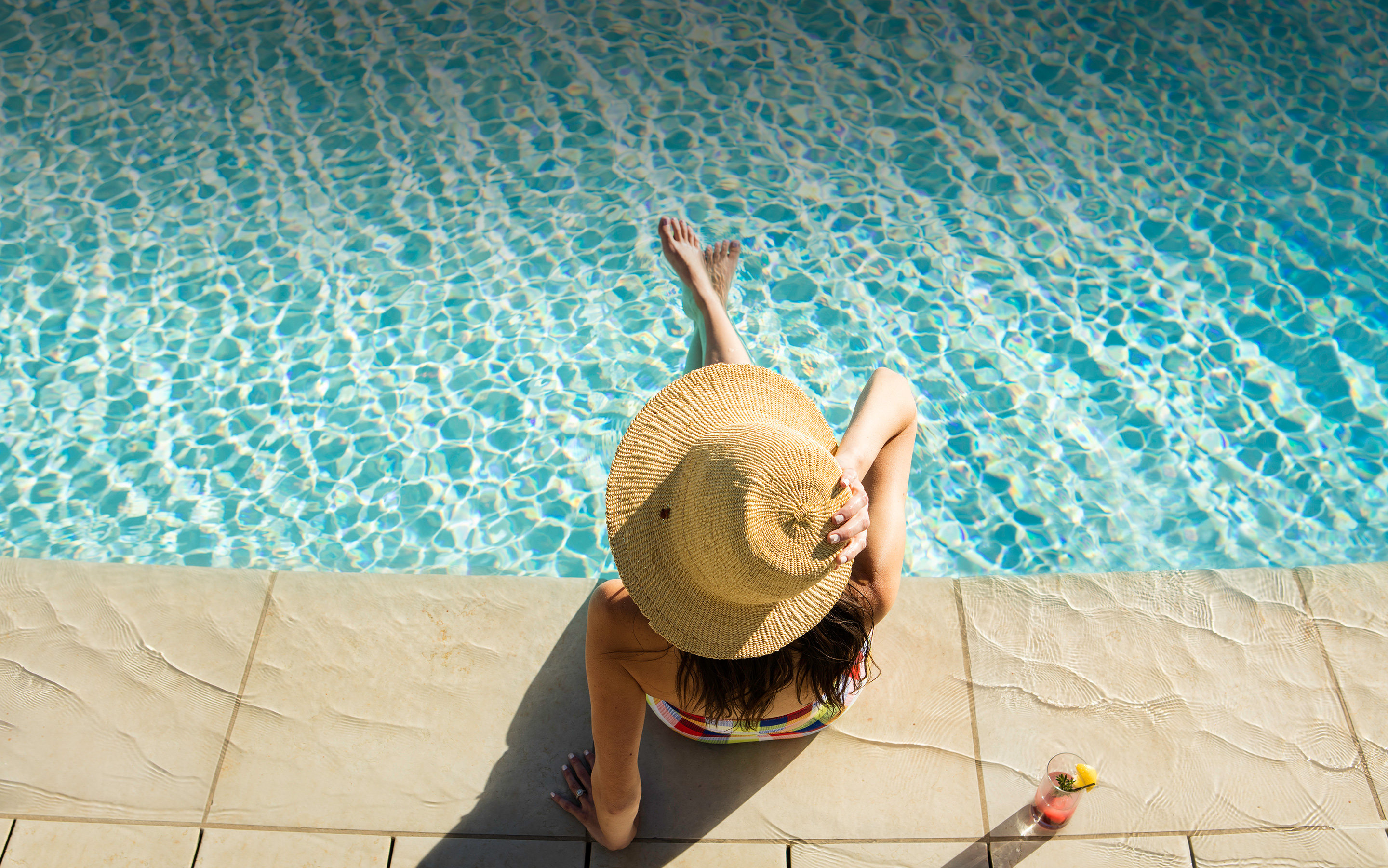 Woman in a hat relaxing in The Grand America Hotel's outdoor pool with a drink
