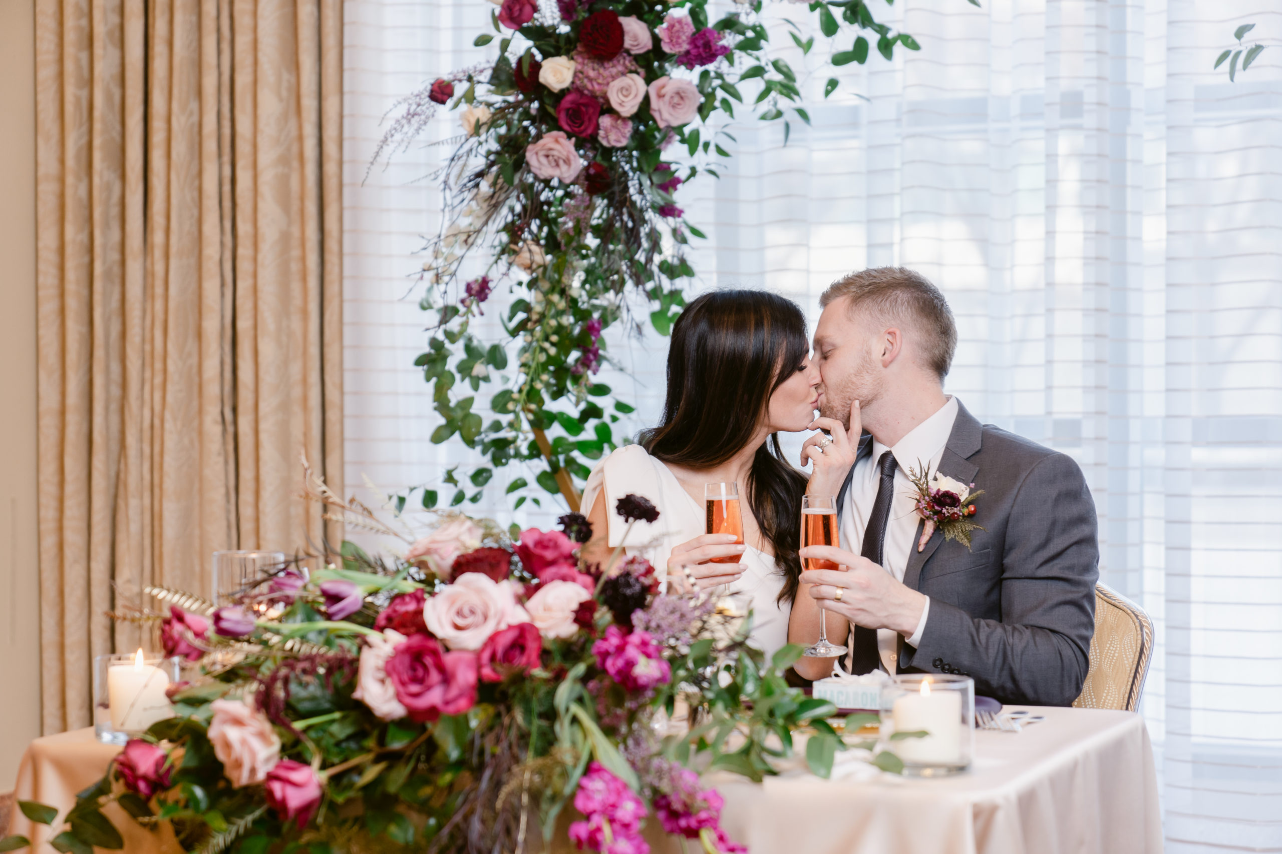Bride and Groom kissing at their Sweetheart's Table decorated with pink and red florals..
