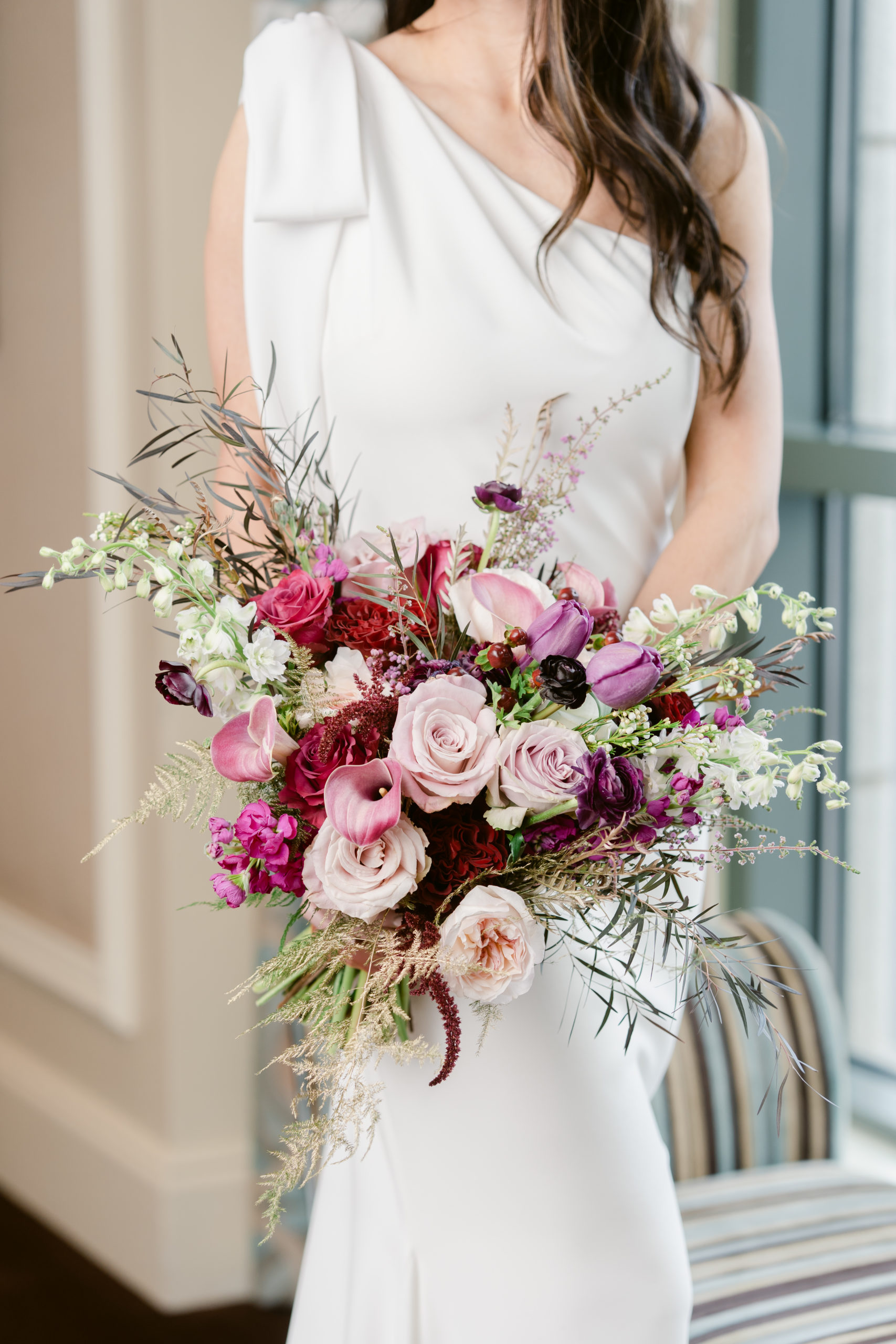 A bride holds her bouquet full of pink, red and purple flowers.