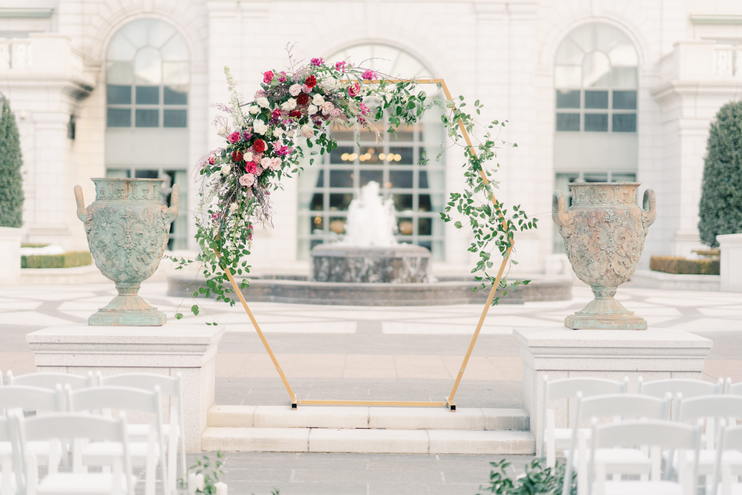 An arch decorated in florals for an outdoor wedding ceremony in the courtyard.