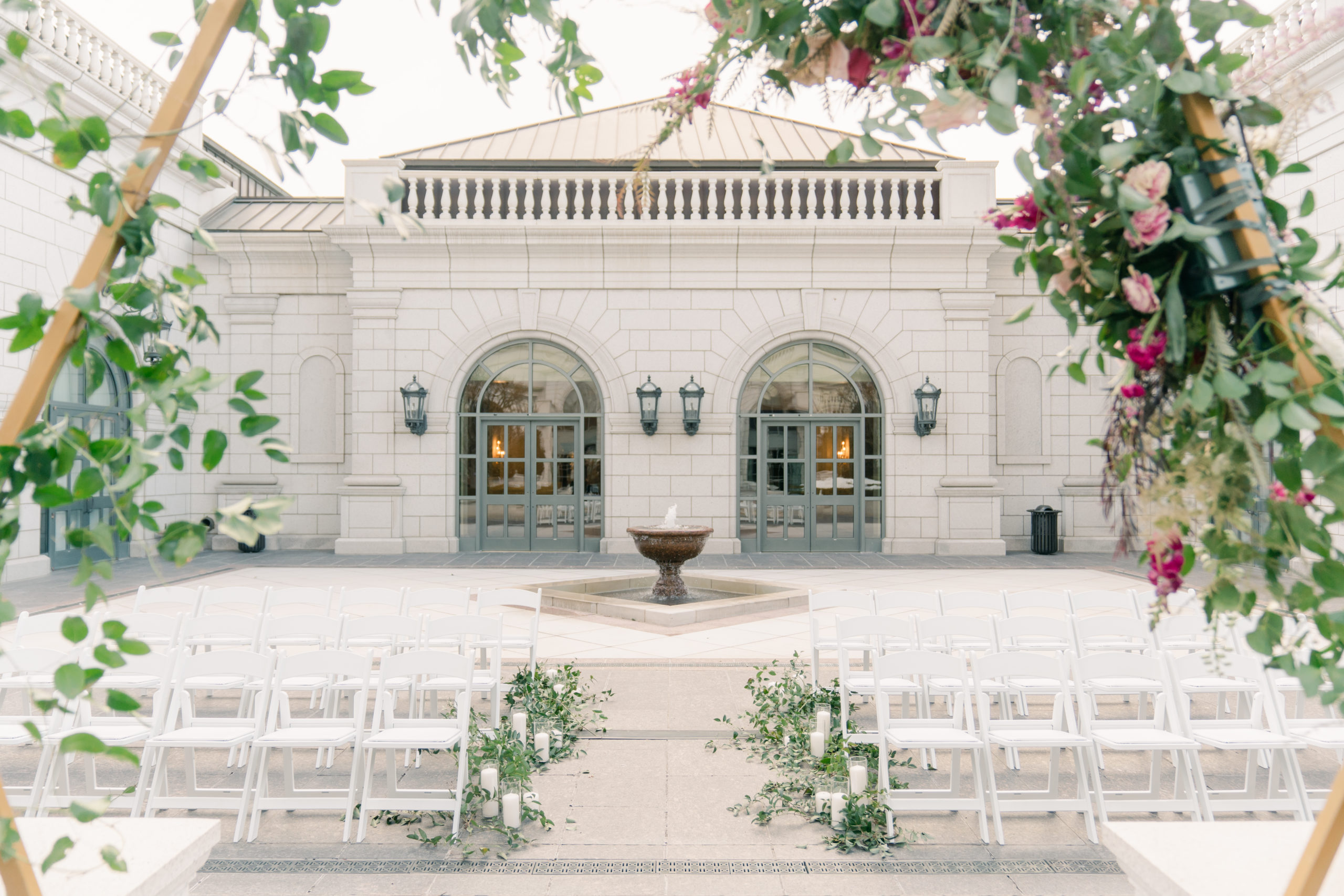 Outdoor wedding ceremony set up with white chairs and greenery in the courtyard.